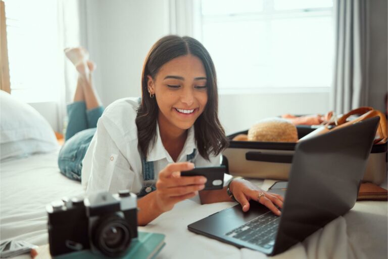 a woman lying on a bed looking at a phone and laptop