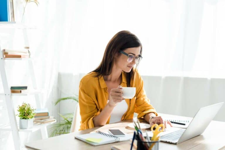 a woman holding a cup of coffee and looking at a laptop