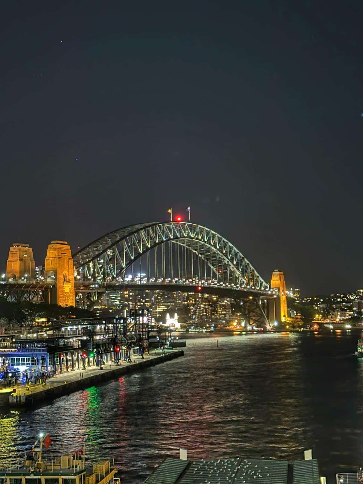 The Sydney Harbour Bridge Lit Up At Night Above The Water
