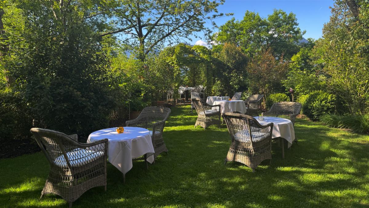 Outdoor Garden Dining At Castel Fragsburg With White-Tablecloth Tables And Wicker Chairs Set Among Lush Trees In Merano, South Tyrol