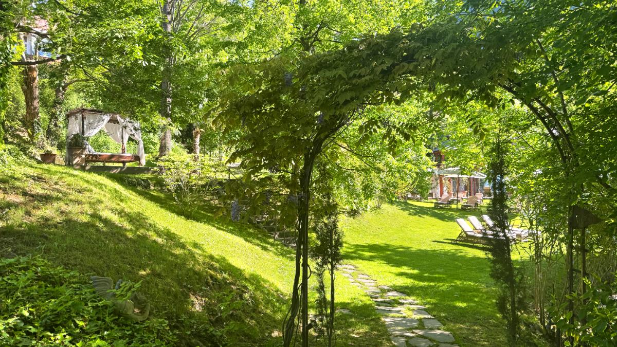 Lush Hotel Garden At Castel Fragsburg With Canopy Daybed, Wisteria Arch, Stone Pathway, And Chaise Lounges In Merano, Italy