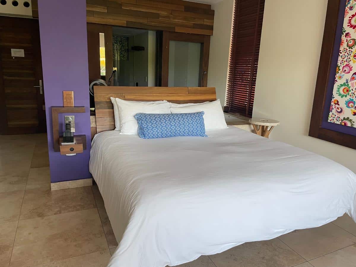 King Suite At Xcaret Arte All-Inclusive Resort With Wooden Headboard, Colorful Mexican Folk Art Window Frame, And Open-Concept Bathroom