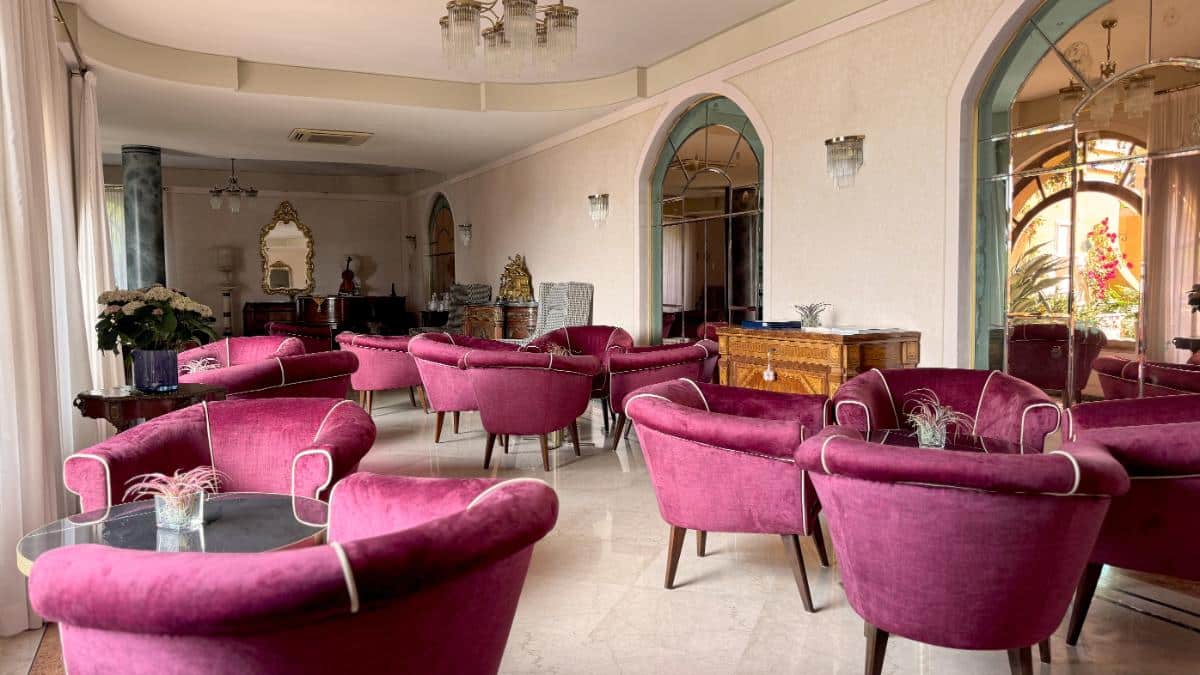 American Bar Lounge At Villa Del Sogno Lake Garda With Plush Magenta Velvet Armchairs, Crystal Chandeliers, And Arched Mirrors