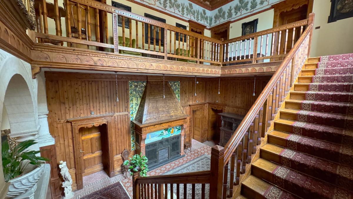 Grand Foyer At Villa Del Sogno Lake Garda With Ornate Carved Wooden Balcony, Stained-Glass Fireplace, And Carpeted Staircase