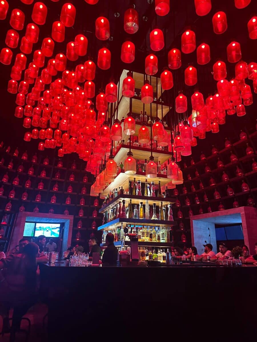 El Deseo Speakeasy Bar At Xcaret Arte Resort With Dramatic Red Glowing Bottle Ceiling Installation And Evening Cocktails