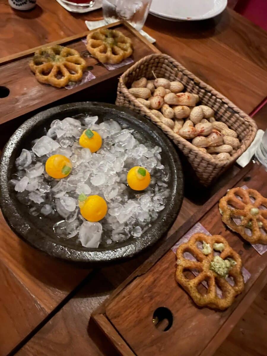 Amuse-Bouche Snacks At Chino Poblano Restaurant At Xcaret Arte — Citrus Spheres On Ice, Fried Lotus Crackers, And Roasted Nuts